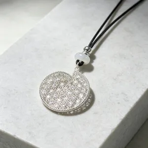 Close-up detail of silver filigree spiral pendant necklace with black cord and elegant beads.