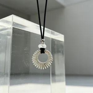 Detail shot of the silver hollow sunburst pendant necklace with white bead on black cord.