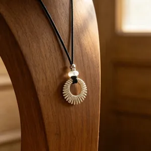 Silver sunburst pendant necklace detail, elegant hollow circular design on black cord.
