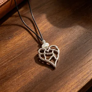 Detailed shot of a silver hollow heart pendant necklace with a black leather cord and pearl.