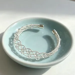 Bracciale rigido intrecciato in argento con perle di cristallo, dettaglio elegante.
