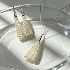Detail shot of elegant pearl tassel jewelry set in glass bowl with sunlight shadows.