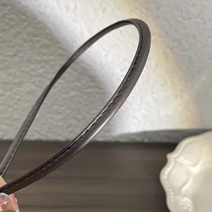 Vue détaillée d'un cerceau de cheveux fin en cuir PU marron foncé montrant une texture et des coutures.
