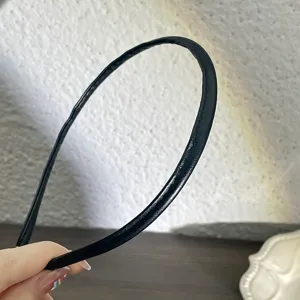 Gros plan détaillé montrant la texture élégante du fin serre-tête minimaliste en cuir PU noir.