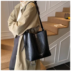 Vue détaillée du sac seau d'épaule noir à motif crocodile porté dans une scène intérieure.