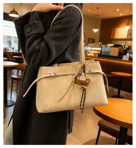 Detailed shot of women's chic beige suede shoulder tote bag with cute bear pendant.