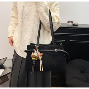 Black suede tote bag with stylish belt detail and cute bear pendant, perfect for daily commuting.