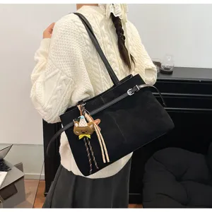 Detailed shot of black suede shoulder bag with cute bear pendant and stylish strap design.