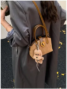 Close-up of stylish retro suede shoulder bag with cute fluffy dog plush charm and elegant lock.