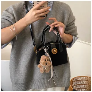 Chic black shoulder bag featuring a cute fluffy bear pendant and gold hardware detail.