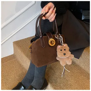 Elegant brown suede handbag with chic twist lock and cute plush bear keychain charm.