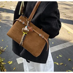 Close-up detail shot of the brown suede shoulder bag featuring a cute bear pendant accessory.