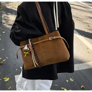 Detail view of brown suede shoulder tote bag with cute charm, ideal for chic daily commuting.