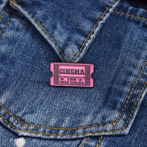 Close-up van roze bioscoopkaartje emaille speld gedetailleerde metalen badge op spijkerjas.
