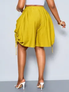Detail view of high-waisted drawstring harem shorts in mustard yellow with large pockets.