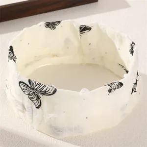 Gros plan d'un bandeau à cheveux en tissu blanc avec des motifs de papillons noirs.