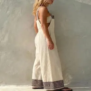 Side view of beige linen geometric embroidered overall jumpsuit, showing wide leg details.
