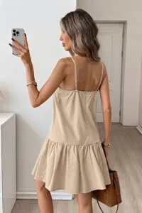 Close-up detail of the elegant beige spaghetti strap mini dress showcasing the ruffled hem.