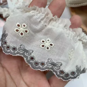 Detail shot of white pleated cotton lace trim with grey butterfly embroidery and eyelet flowers.