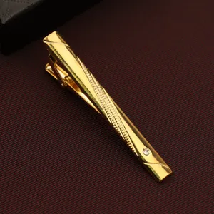 Gold metal tie clip detail shot featuring diagonal textured pattern and embedded crystal stone.