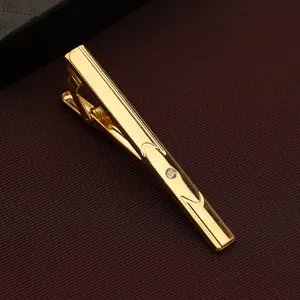 Detailed close-up of a classic gold tie clip with engraved lines and sparkling crystal accent.