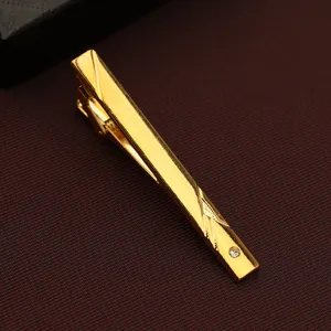 Detailed close-up of a stylish gold metal men tie clip with geometric engraving and rhinestone.