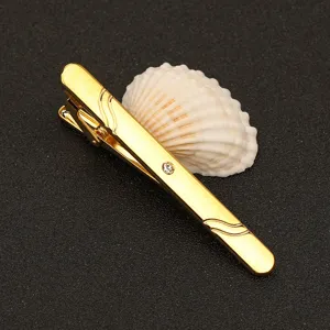 Detalle de pinza de corbata dorada con elegante patrón de ondas y brillante strass.