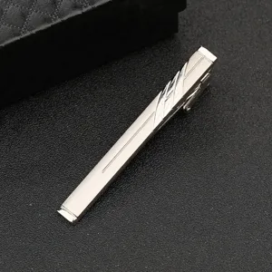 Close-up detail shot of a sleek silver metal tie clip featuring elegant linear engraved patterns.