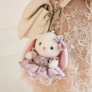 Close-up of a cute white plush rabbit keychain in a purple floral dress hanging on a bag.
