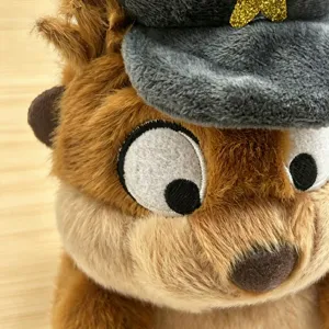 Close-up detail shot of cute plush toy head with soft brown fur, embroidered eyes and cap.