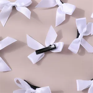 Detail view of white ribbon bow hair clips, showing polyester fabric and metal alligator clip texture.