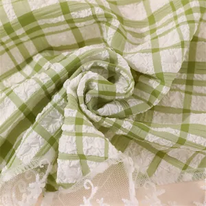 Green and white plaid fabric detail with white lace trim, close-up shot of texture.