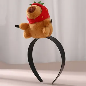 Close-up detail of the cute capybara plush doll wearing a strawberry hat on a black headband.