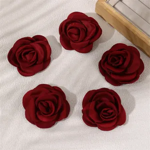 Detailed close-up of dark red fabric rose hair clips arranged on a textured white background.