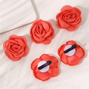 Close-up detail shot of red fabric rose hair clips showing the back duckbill clip structure clearly.