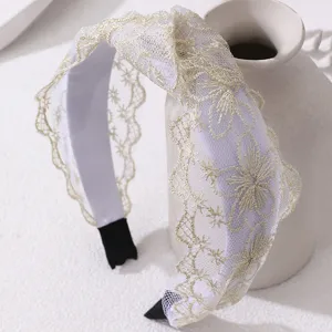 Detailed close-up shot of elegant white mesh headband featuring delicate gold floral lace embroidery.