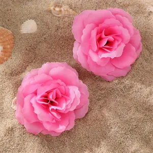 Gros plan detail de pinces a cheveux en tissu fleur rose degrade sur fond de plage de sable fin.