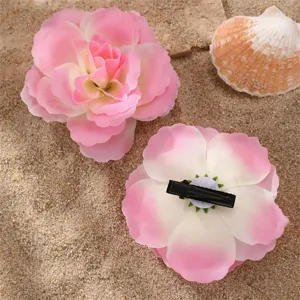 Gros plan de pinces à cheveux en tissu fleuri dégradé rose avec pince bec de canard sur sable.
