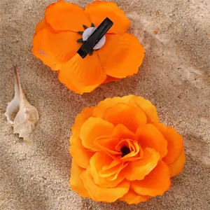 Détail de pince à cheveux fleur en tissu dégradé orange, style doux sur fond de sable.