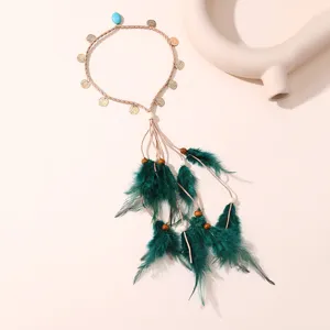 Détail de bandeau en plume bohème avec cordon tressé, pièces dorées et plumes vertes.