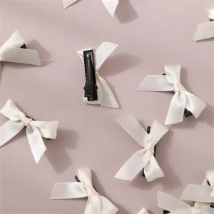 Close-up detail of beige ribbon bow hair clips, showing delicate fabric texture and metal clip.