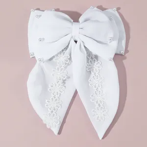 White fabric hair bow with pearl accents and delicate lace streamers for bridal wear detail.