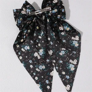 Close-up detail of the black floral fabric bow hair clip showing texture and clasp.