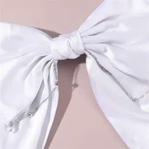 White satin bow hair clip close-up detail showcasing delicate metal chains and pearl pendant.