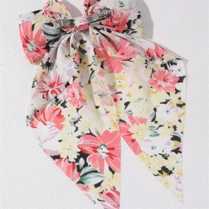 Close-up detail of floral fabric hair bow barrette with long ribbons and metal clip.