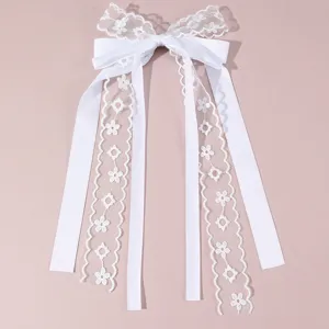 White lace bow hair clip detail shot showing delicate floral embroidery and long satin streamers.
