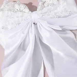Close-up detail of white satin bow hair clip with delicate lace and pearl embellishments.