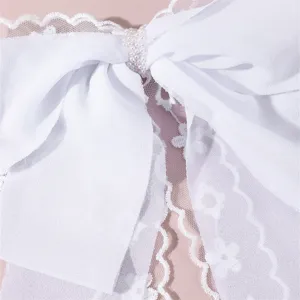 Close-up detail of white fabric bow hair clip with delicate lace ribbon and elegant pearl center.