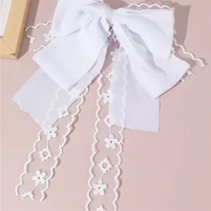 Close-up detail of white fabric bow hair clip with delicate lace ribbons and pearl accent.