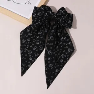 Detailed shot of black floral fabric bow hair clip, featuring long streamers and spring clasp.